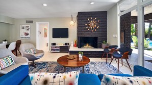 A modern living room with a fireplace, comfortable seating, a flat-screen TV, and a large window.