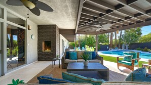 A covered patio area with outdoor furniture, a stone fireplace, and a view of a swimming pool.
