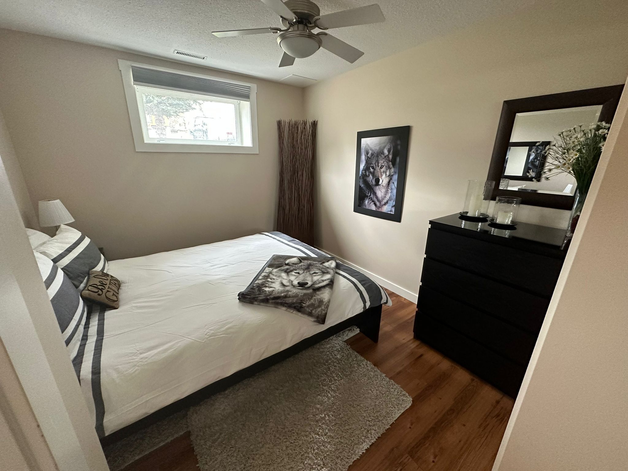 A bedroom with a bed, a dresser, a ceiling fan, a window, and a framed picture on the wall.