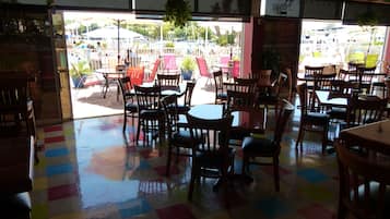 An indoor dining area with tables and chairs, a colorful floor, and a view of an outdoor pool area.