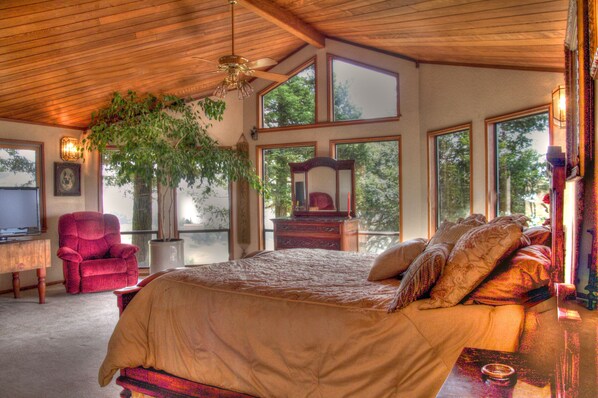 A spacious bedroom with a large bed, a red armchair, a wooden ceiling, and large windows offering a view of trees. - The Gated Country Estate | High Elevation| Views| Weddings (Fee Applies) (Livermore)