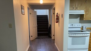 A narrow hallway with wooden flooring, a white stove, and a fire extinguisher on the wall. - Whale Cove suites (Whale Cove)