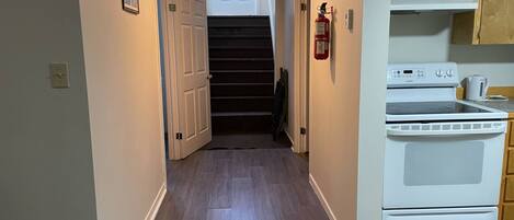 A narrow hallway with wooden flooring, a white stove, and a fire extinguisher on the wall.
