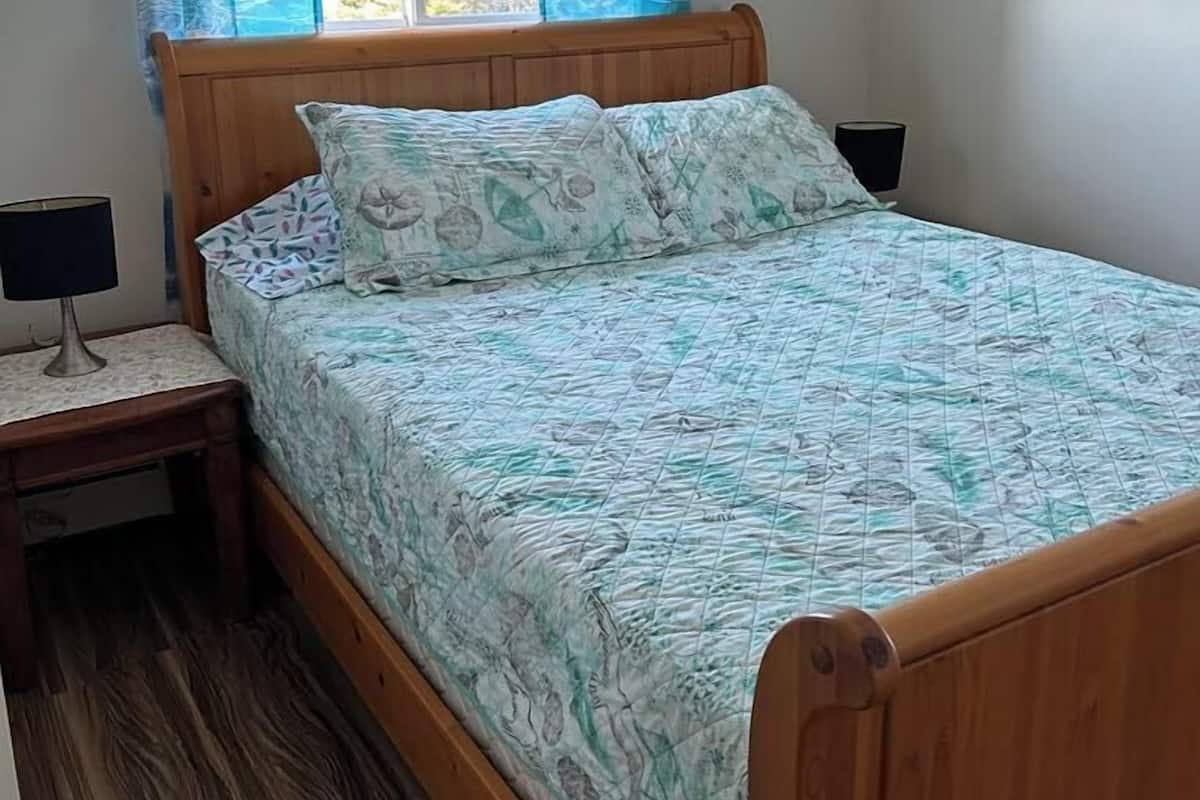 Un dormitorio con cama de madera, mesita de noche, lámpara y ventana con cortinas azules.
