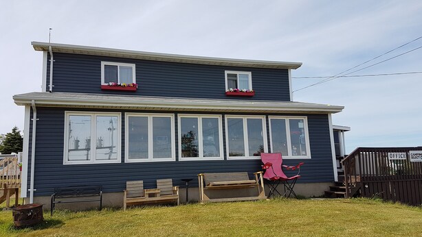 A two-story house with large windows, a red chair, and a bench outside. - Whale Cove suites (Whale Cove)