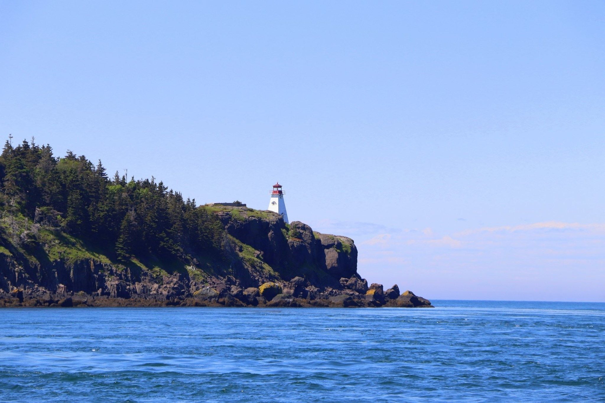 A lighthouse on a rocky cliff with a clear view of the ocean.