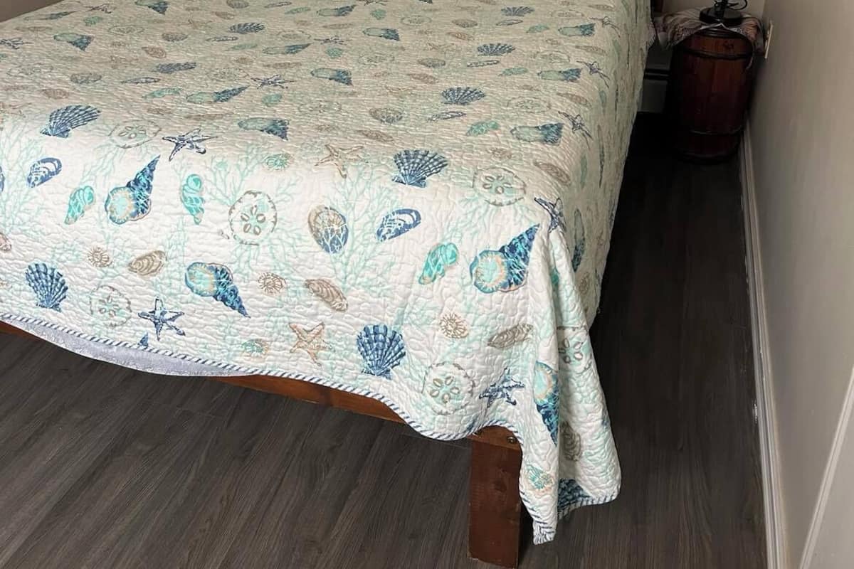 Una cama con una colcha estampada, un cabecero de madera, una mesita de noche con una lámpara y un piso de madera oscura.