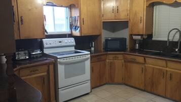 Una cocina con armarios de madera, estufa, microondas y una ventana con persianas.