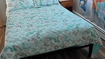 A bed with a patterned bedspread, a nightstand with a lamp, and a window with a curtain.