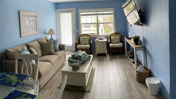 A living room with a blue wall, a sofa, a coffee table, a chair, a television, and a window. - Relaxing Beach Getaway (Bradenton Beach)