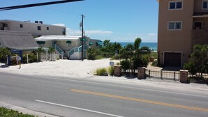 Uma estrada costeira com uma propriedade à beira-mar, portão de entrada, placa indicando acesso à praia e vista para o oceano.