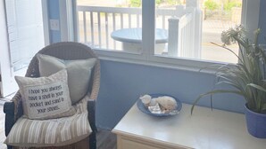 Um quarto com uma cadeira de vime, um console branco e uma janela com vista para o mar.