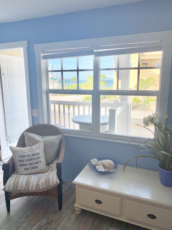 A room with a wicker chair, a white console table, and a window with a view of the sea.