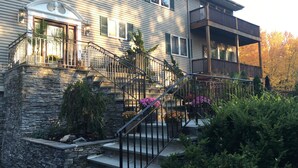 A two-story house with a stone foundation, a front porch with a staircase, and a balcony on the second floor. - Beautiful Saugerties Rental -Pool, Fire Pit, close to HITS, Hiking, Festivals (Saugerties)