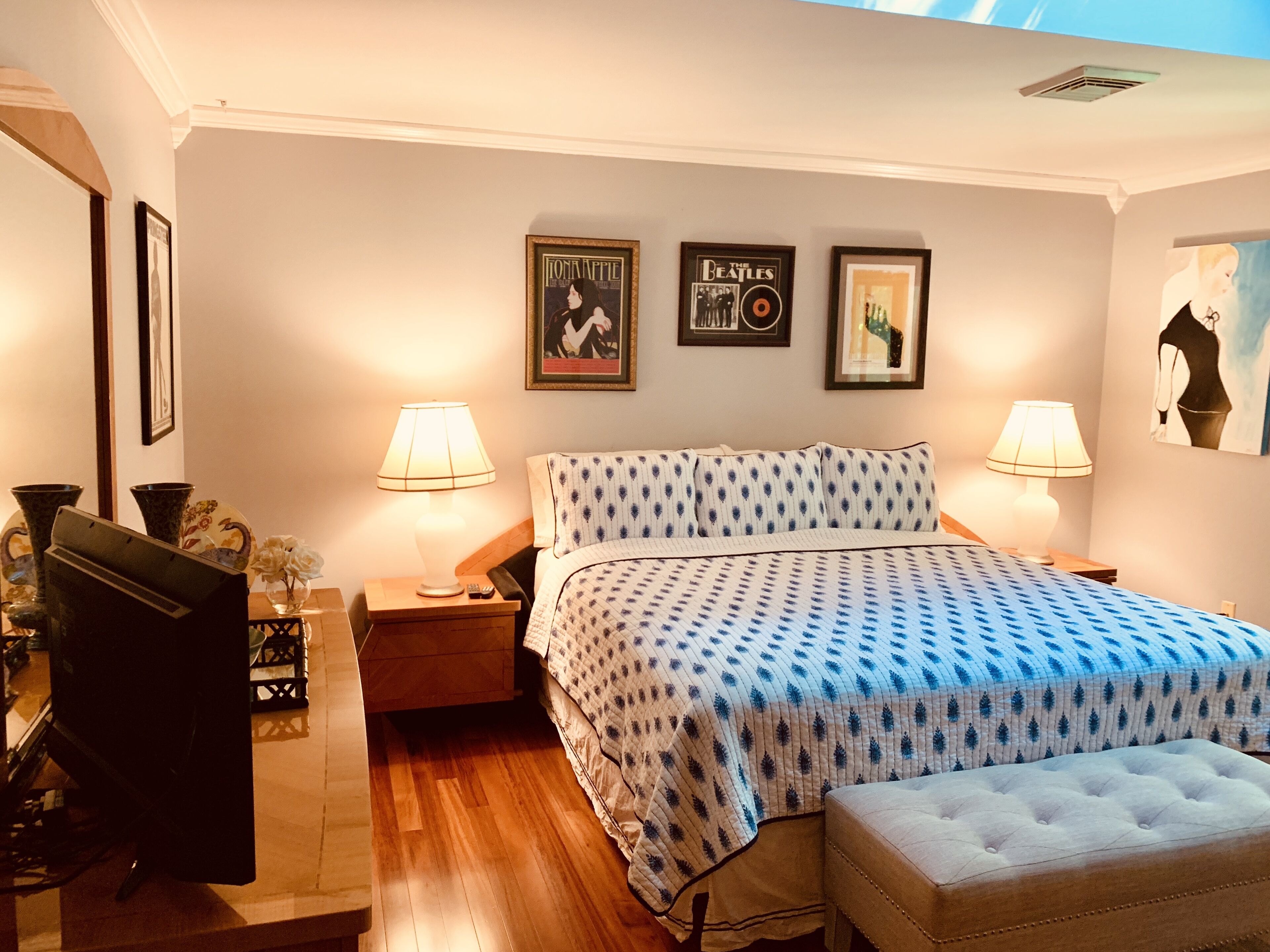 Une chambre à coucher avec un lit, deux lampes de chevet, une table de chevet, une commode et des affiches encadrées accrochées au mur.