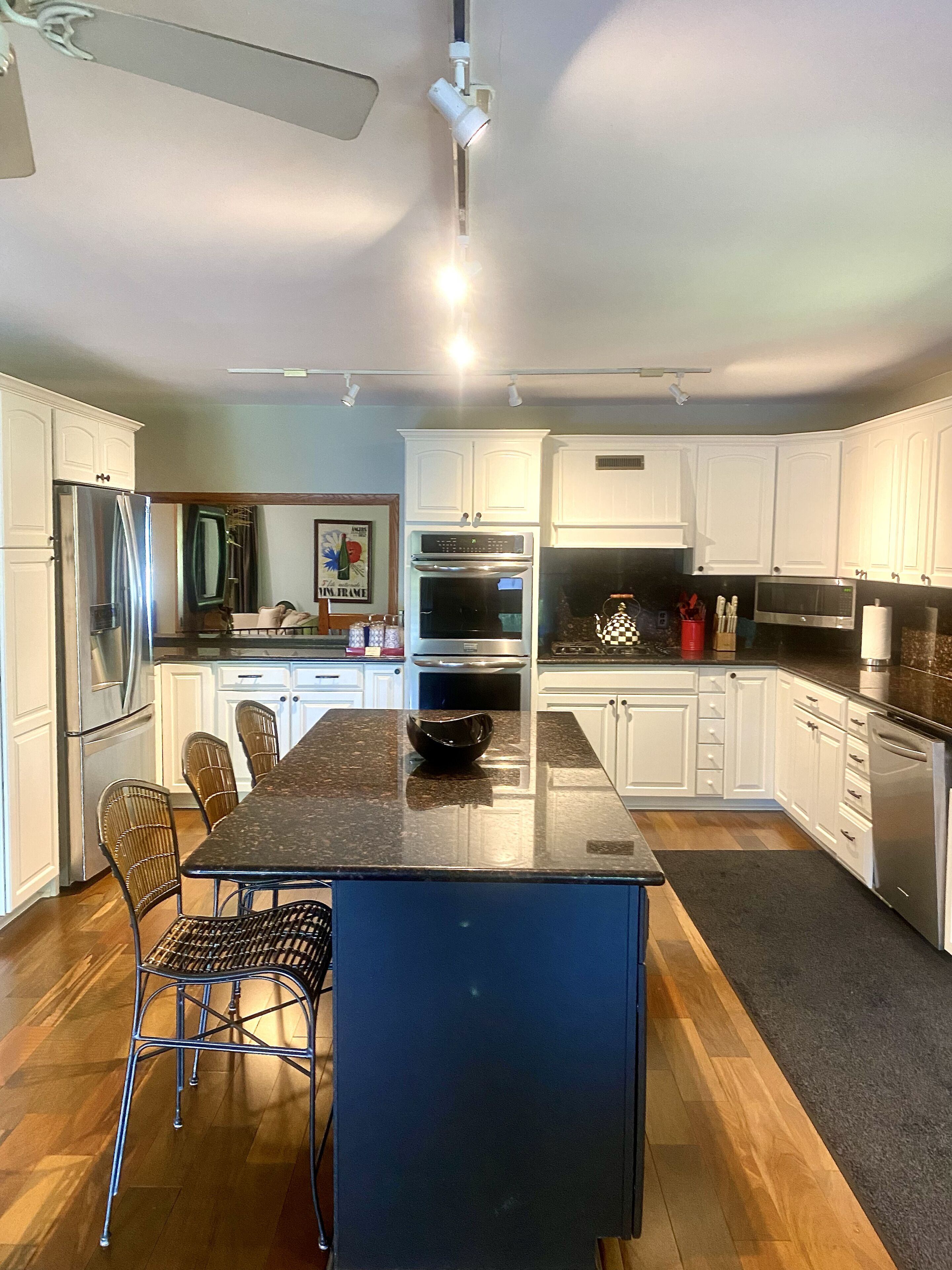 A modern kitchen with white cabinets, stainless steel appliances, a granite countertop, and a dining area with metal chairs.