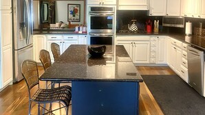 A modern kitchen with white cabinets, stainless steel appliances, a granite countertop, and a dining area with metal chairs. - Beautiful Saugerties Rental -Pool, Fire Pit, close to HITS, Hiking, Festivals (Saugerties)