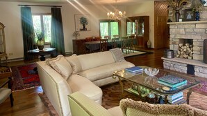 A spacious living room with a large sectional sofa, a glass coffee table, and a fireplace. There is a dining area in the background with a chandelier. - Beautiful Saugerties Rental -Pool, Fire Pit, close to HITS, Hiking, Festivals (Saugerties)