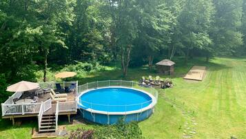 A circular pool with a wooden deck and a white railing, surrounded by a well-maintained lawn and trees.