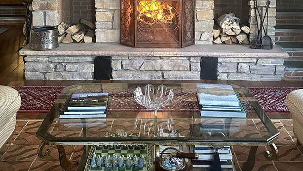 A stone fireplace with a fire, surrounded by decorative items and a glass coffee table with books and chess pieces. - Beautiful Saugerties Rental -Pool, Fire Pit, close to HITS, Hiking, Festivals (Saugerties)