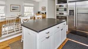 Eine moderne Küche mit weißen Schränken, einem Edelstahl-Kühlschrank und einem Essbereich mit weißen Stühlen und einem Holztisch.