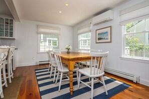 A dining area with a wooden table and white chairs, a blue and white striped rug, and a picture on the wall.