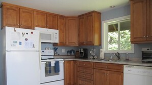A kitchen with wooden cabinets, a white refrigerator, a stove, and a dishwasher. - Bass Harbor Oceanfront Chalet:  Peaceful, Private, Great On-The-Ocean View (Bass Harbor)