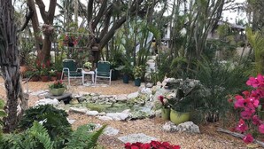 Ein Garten mit einem kleinen Teich, Blumentöpfen und einer Sitzgelegenheit mit Stühlen und Tischen.