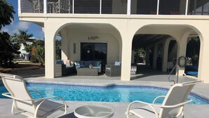 Ein Poolbereich mit Liegestühlen und einem Glastisch, umgeben von einer überdachten Terrasse mit Sitzgelegenheiten und einer dekorativen Fischskulptur.