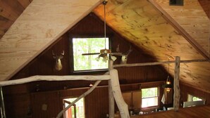 Una cabaña de madera rústica con techo inclinado, un área de loft con ventana y cornamentas de ciervo montadas en las paredes.