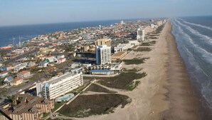 An aerial view of a coastal city with a long beach, buildings, and a clear sky. - Casa Del Sol I - Large Single-Family Home With Private Pool  (South Padre Island)