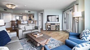 Un salon spacieux avec un canapé, une table basse et un meuble pour la télévision. On y trouve un lustre, une horloge et une lampe.