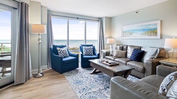 Un salon avec vue sur l’océan, comprenant deux fauteuils bleus, un canapé marron et une table basse.