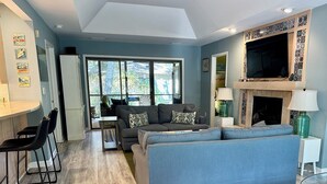 Un salon moderne avec un canapé, un téléviseur et une cheminée. On y trouve également un coin repas avec des chaises et une table.
