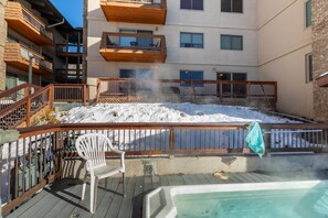 Una terraza con un jacuzzi, barandas de madera y una silla.