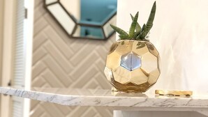 Ein modernes Interieur mit einer Marmorarbeitsplatte, einer sechseckigen, goldenen Vase mit Pflanze und einem geometrischen Spiegel an der Wand.