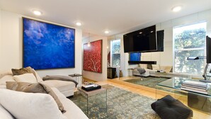 Ein modernes Wohnzimmer mit einem großen, blauen, abstrakten Gemälde, einem Glastisch und einer Couch mit Kissen.