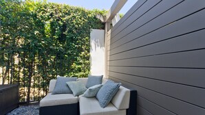 Eine Terrasse mit bequemen Sitzmöbeln, Steinboden und einem Hecken im Hintergrund.