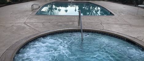 A hot tub with a tiled edge and a pool in the background.