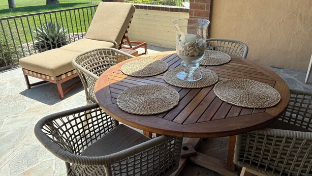 Une terrasse dotée de meubles en osier, d’une table ronde en bois et d’un bol en verre rempli de pierres.