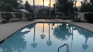 Une piscine rectangulaire à l’eau claire, dans laquelle se reflètent les palmiers et les couleurs d’un coucher de soleil.