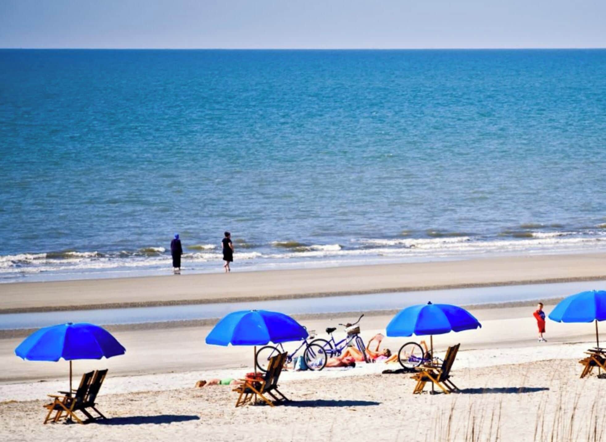 Uma praia com guarda-sóis, cadeiras e bicicletas.
