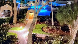 Une vue nocturne d’un complexe hôtelier, avec des arbres illuminés et un espace piscine.