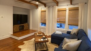 Uma sala de estar moderna com teto de madeira, televisão de tela plana, sofá azul e mesa de centro.