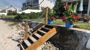 A wooden staircase leading down to a sandy beach, surrounded by rocks and a 'PRIVATE BEACH' sign.