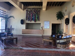 A spacious lobby with a wooden reception desk, seating area, and a wall decorated with colorful tassels.