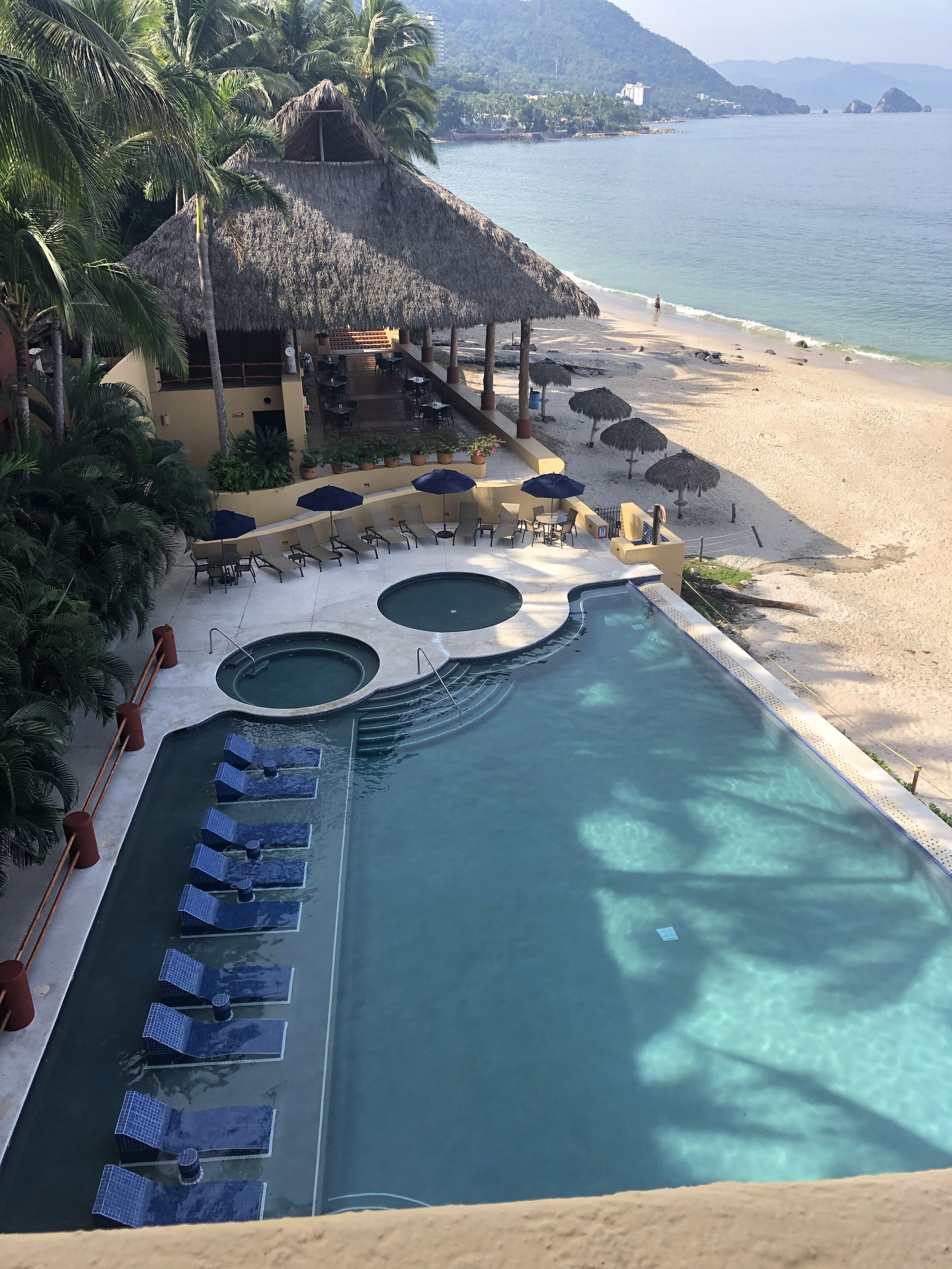 A resort pool with lounge chairs and umbrellas, a beach, and palm trees.