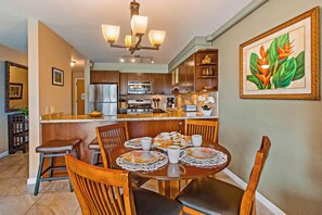 A modern kitchen with a dining area, featuring a central island, wooden chairs, and a chandelier. - Quiet Kihei 4th Floor Condo Hawaiian Decor Cal King Lanai Ocean Views Pool (Kihei)