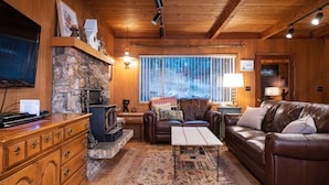 Ein gemütliches Blockhaus-Interieur mit Kamin aus Stein, Ledermöbeln und einem an der Wand befestigten Fernseher.
