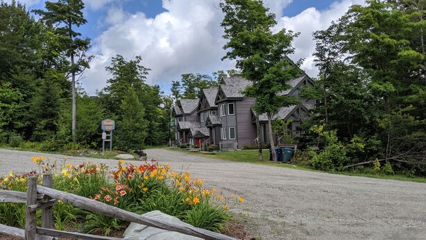 A row of traditional wooden houses with a gravel driveway and a sign indicating 'Village of' and 'Rural'.